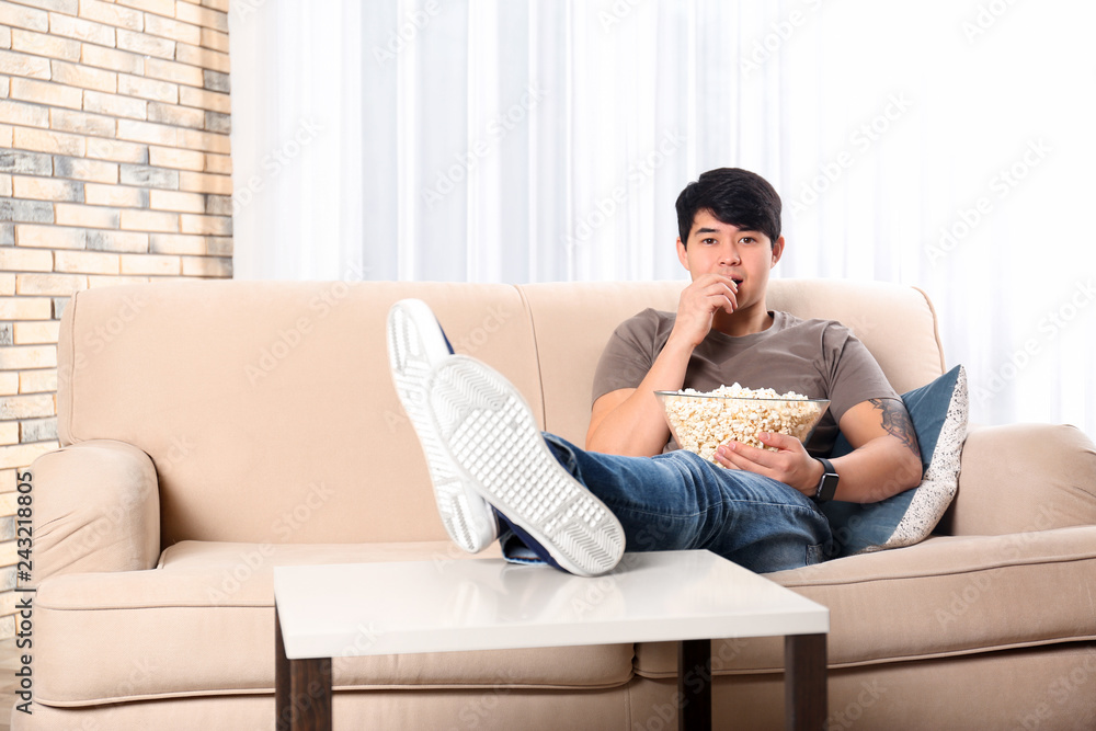 Young man with bowl of popcorn watching TV on sofa at home Young man with bowl of popcorn watching TV on sofa at home