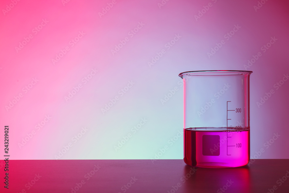 Beaker with liquid on table against color background. Chemistry laboratory glassware Beaker with liquid on table against color background. Chemistry laboratory glassware