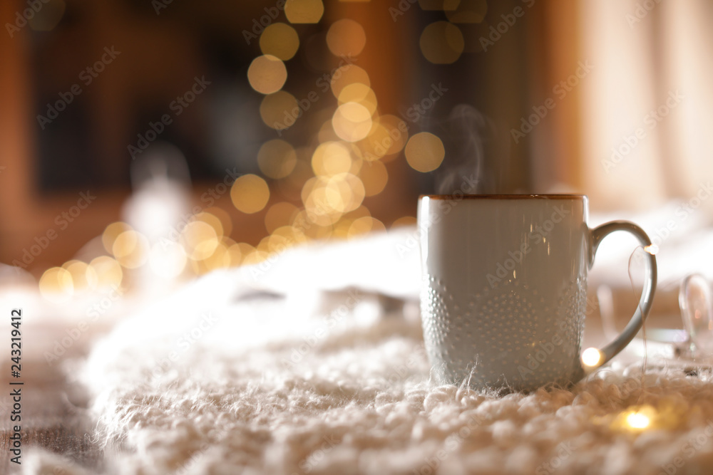 Cup of hot beverage on fuzzy rug against blurred background, space for text. Winter evening - obrazy, fototapety, plakaty 
