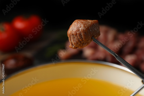 Fried piece of meat on fondue fork against blurred background. Space for text