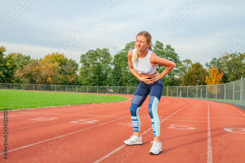 Woman on running track has side cramps during workout © Dmytro Flisak