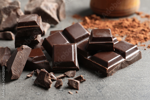 Pieces of chocolate and cocoa powder on grey background, closeup