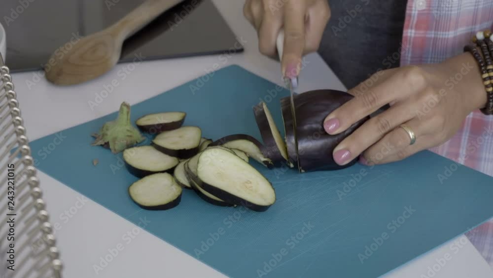 Female hands cutting fresh eggplant with knife. Young woman cooking at kitchen table. Cooking concept Female hands cutting fresh eggplant with knife. Young woman cooking at kitchen table. Cooking concept