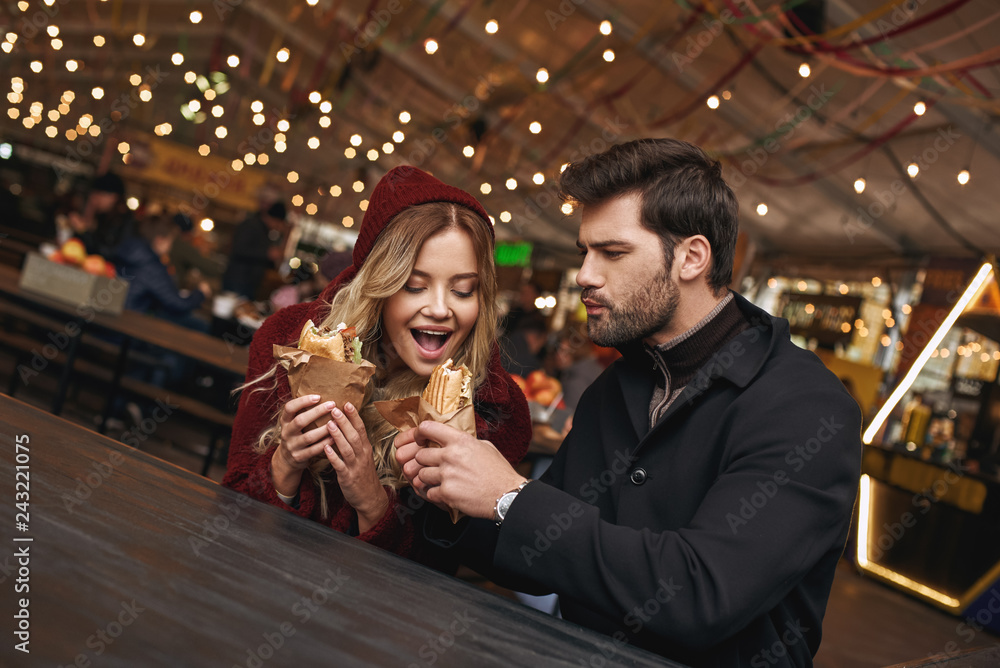 Close-up of young couple are eating sandwiches at the street food market. Close-up of young couple are eating sandwiches at the street food market.