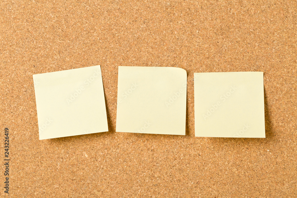 Three empty yellow sticky paper memo notes on cork board Three empty yellow sticky paper memo notes on cork board