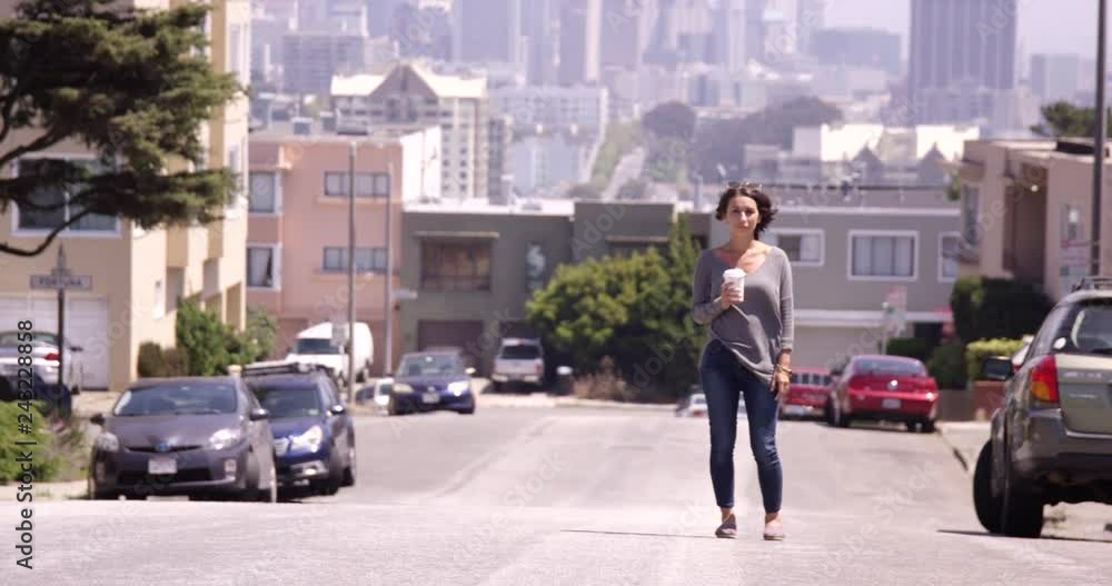 Woman standing in middle of street with coffee cup in hand with a city scape behind her - wide shot Woman standing in middle of street with coffee cup in hand with a city scape behind her - wide shot