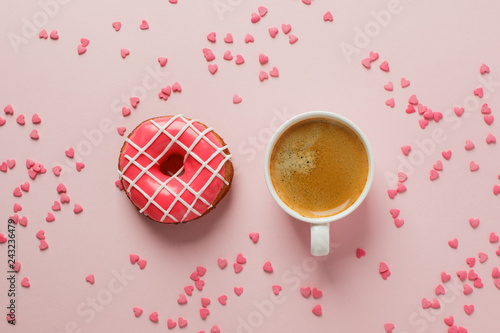Morning coffee cup and sweet pastry of pink berry donut and heart shaped sprinkles on pink pastel table top view. Flat lay. Cozy romantic breakfast photo