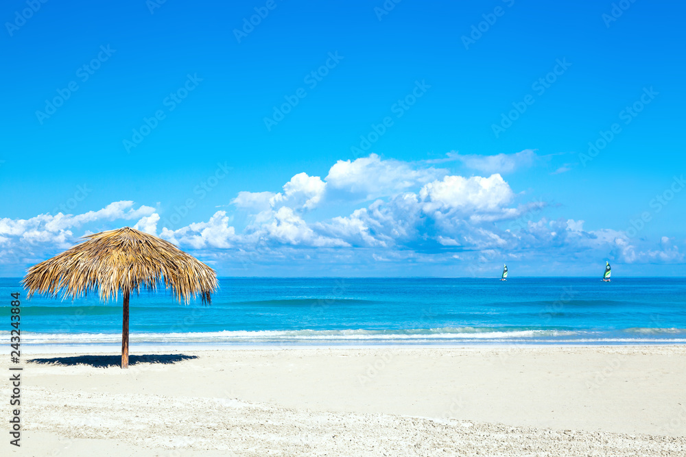 Straw umbrella on empty seaside beach in Varadero, Cuba. Amazing blue sky with clouds. Relaxation, vacation idyllic background.