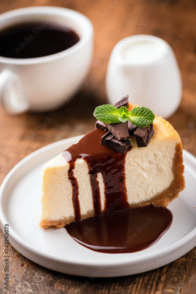 Cheesecake with chocolate sauce and cup of black coffee with cream on wooden table. Selective focus Cheesecake with chocolate sauce and cup of black coffee with cream on wooden table. Selective focus