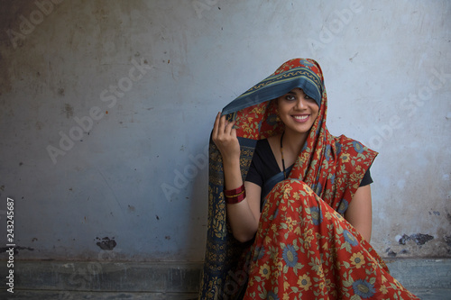 Closeup of a beautiful smiling woman sitting on the floor covering her head with saree.	 photo