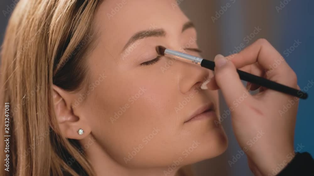 The make-up artist puts bright eye shadow on the eyelids, with a professional brush on the face of a Caucasian blonde model. Close-up, make-up business woman. Slow Motion. The make-up artist puts bright eye shadow on the eyelids, with a professional brush on the face of a Caucasian blonde model. Close-up, make-up business woman. Slow Motion.