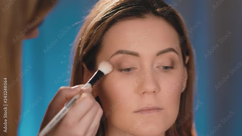 The make-up artist puts dark shadows on the eyelids, a professional white brush on the face of a Caucasian blonde model. Close-up, make-up business woman. Slow Motion. The make-up artist puts dark shadows on the eyelids, a professional white brush on the face of a Caucasian blonde model. Close-up, make-up business woman. Slow Motion.