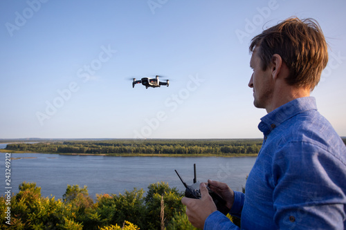 A man launches quadcopter. Flying drone over the river and forest on a sunny day