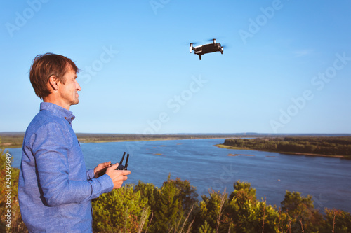 A man launches quadcopter. Flying drone over the river and forest on a sunny day