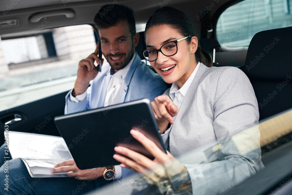 Young business people working together while traveling by a car. Businesswoman received good news via mail and shared with her male colleague.