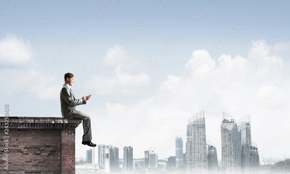 Man on roof edge send message with smartphone and cityscape at background Man on roof edge send message with smartphone and cityscape at background
