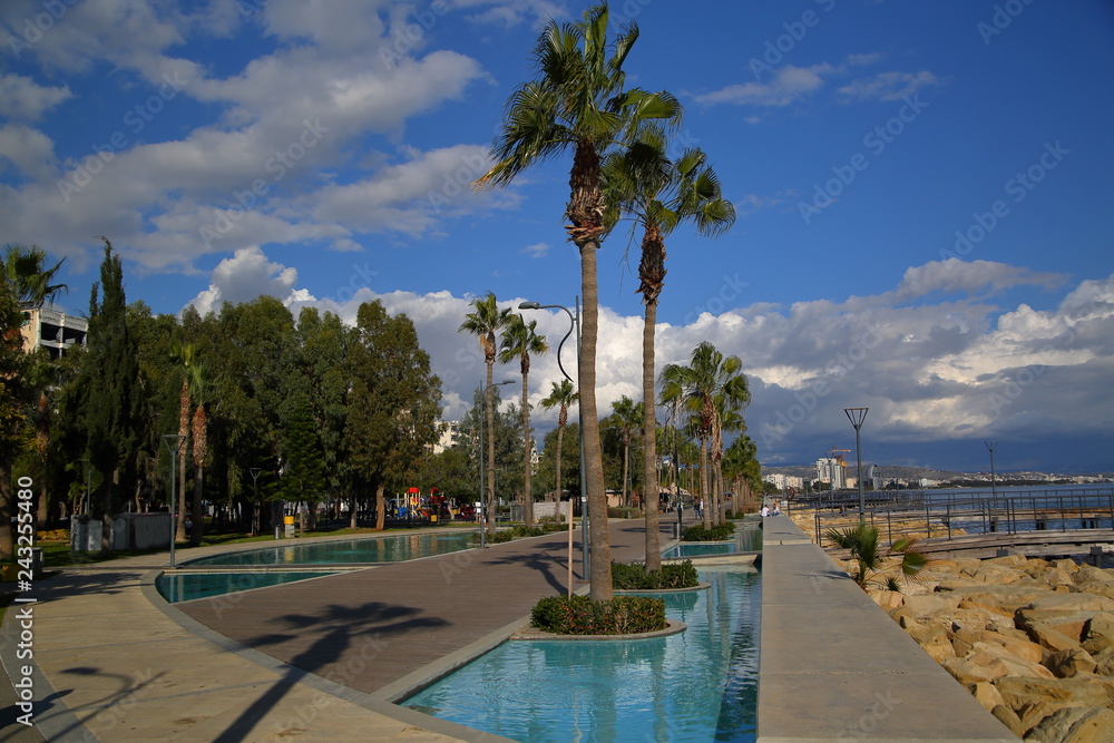 Promenade along sea in Limassol, Cyprus, rocky shore, high palms in park, big basins with beautifully blue water
