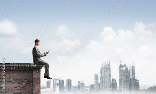 Man on roof edge send message with smartphone and cityscape at background