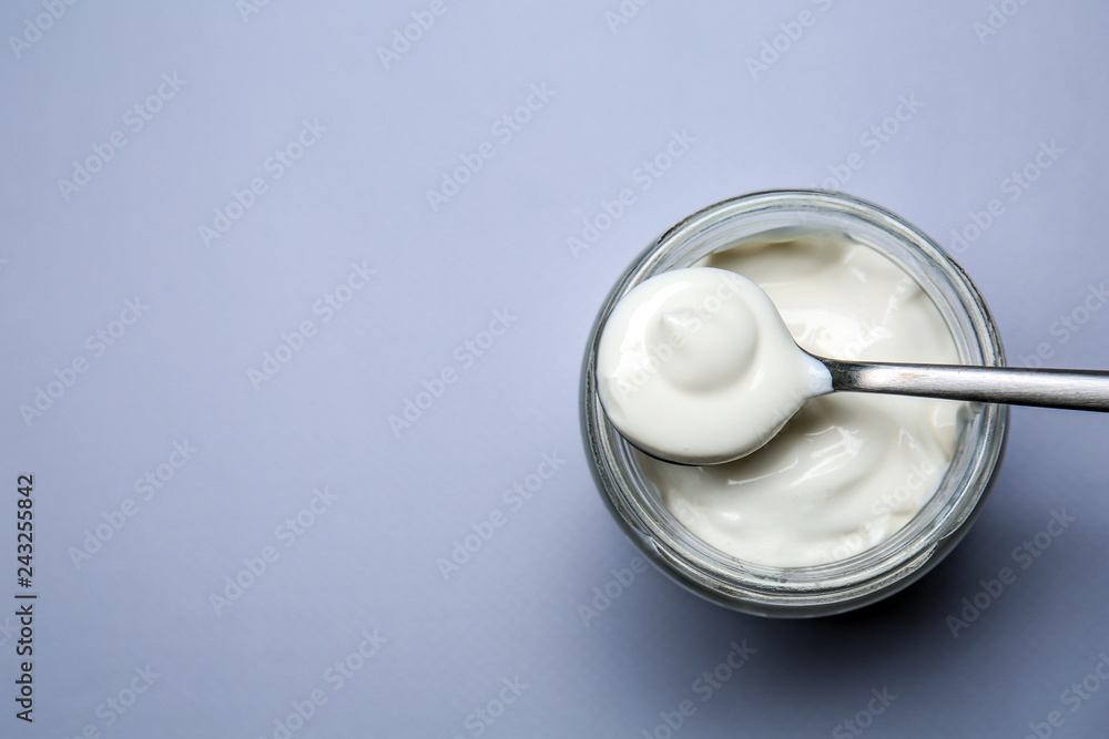Glass jar and spoon with tasty yogurt on light background Glass jar and spoon with tasty yogurt on light background