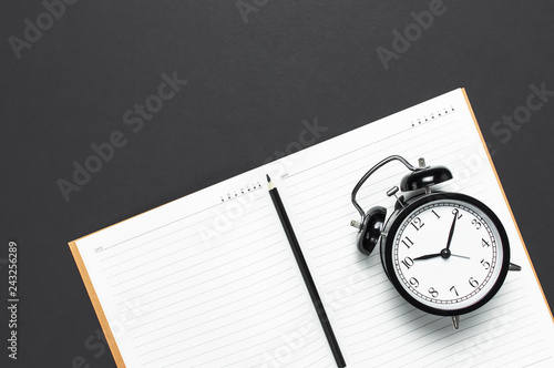 Flat lay black alarm clock, clean open notebook diary, pencil on gray dark background top view copy space. Concept time to work, desktop, Office desk, Minimalistic background for blog