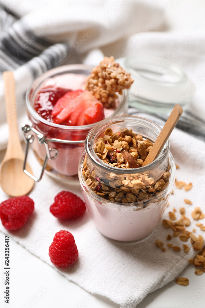 Glass jars of tasty yogurt with jam, strawberry, oatmeal and candied nuts on table Glass jars of tasty yogurt with jam, strawberry, oatmeal and candied nuts on table