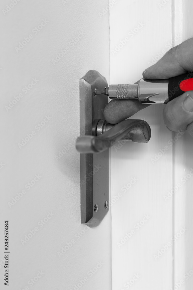 Man tightening a screw on a door handle with a screwdriver with selective colour Man tightening a screw on a door handle with a screwdriver with selective colour