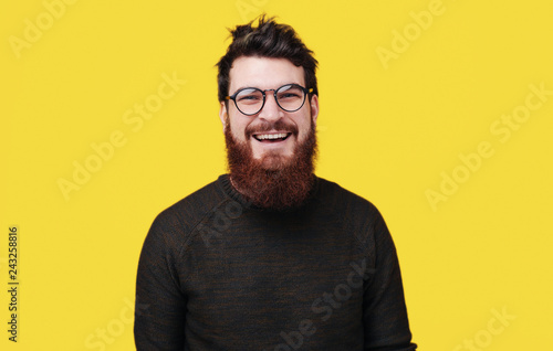 Handsome smiling bearded man standing over yellow background