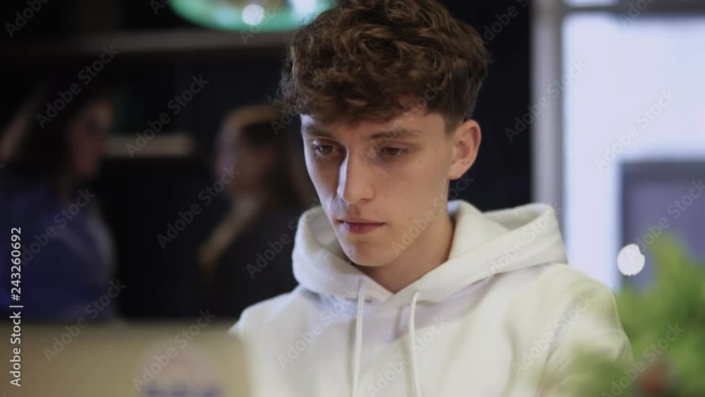 Portrait of young focused guy working in front of a laptop and drinking coffee from paper cup Portrait of young focused guy working in front of a laptop and drinking coffee from paper cup