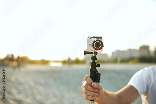 Young man holding an action camera at the desert. Empty space