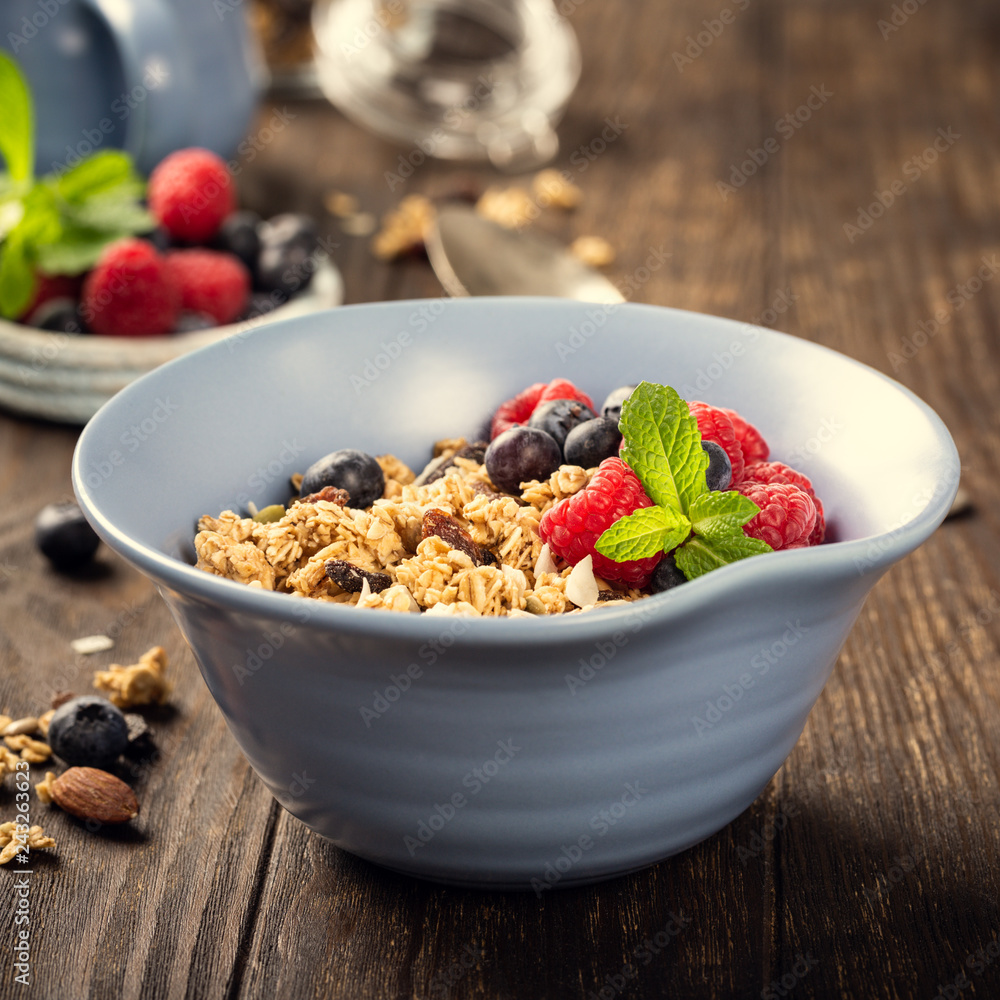 Oat granola with berries and yoghurt in blue bowl on dark old wooden background. Copy space. Healthy breakfast concept. Oat granola with berries and yoghurt in blue bowl on dark old wooden background. Copy space. Healthy breakfast concept.