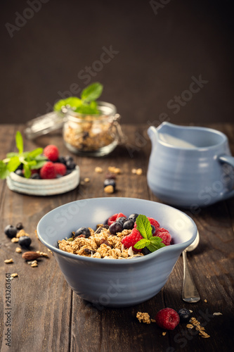 Oat granola with berries and yoghurt in blue bowl on dark old wooden background. Copy space. Healthy breakfast concept.