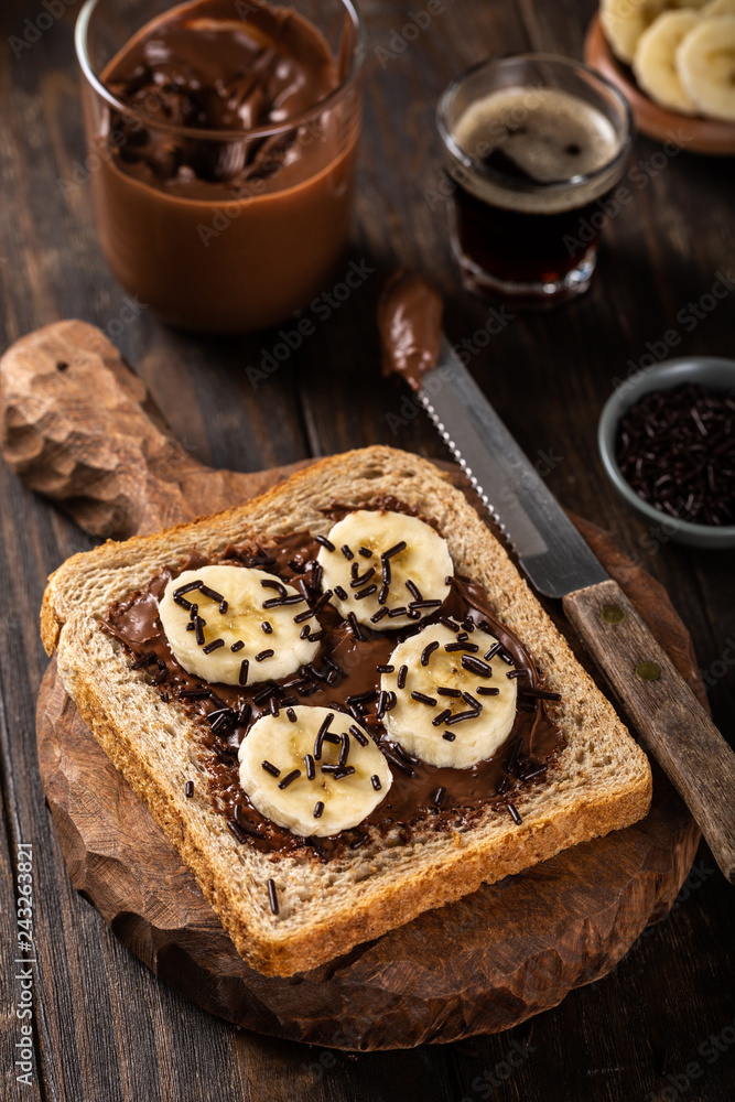 Delicious open sandwich with chocolate and banana on old wooden board and dark table. Breakfast background.