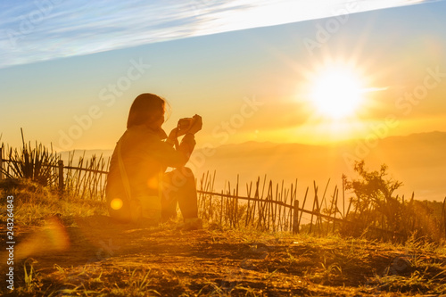 silhouette of female traveler taking photo of beautiful sunrise and mountains with blue sky in the morning, chiang mai in thailand