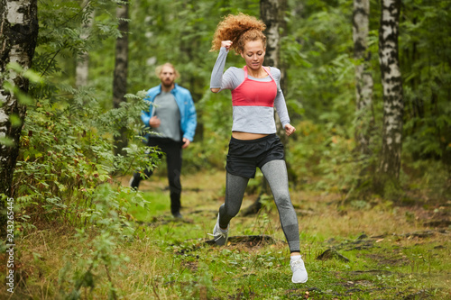 Young active couple in sportswear running in natural environment on summer morning before workout