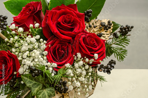 
A small wooden box with a bouquet of red roses surrounded by branches of white gypsophila, berries and coniferous twigs