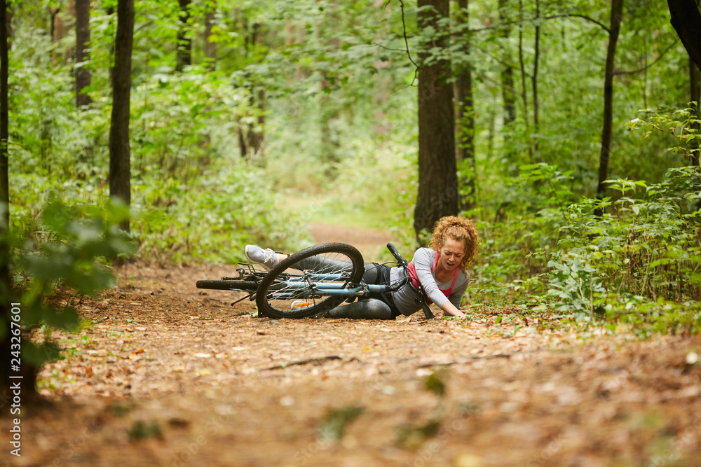 Fototapeta Młoda sportsmenka spadła z roweru i raniła nogę na leśnej ścieżce podczas porannej jazdy