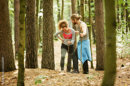 Obraz na plátně Young sportsman helping his girlfriend with hurting leg to walk in the forest af