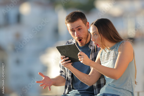 Amazed friends finding online content on a tablet outdoors