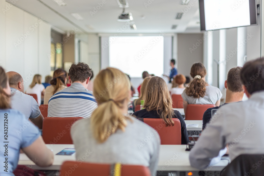 Female speaker giving presentation in lecture hall at university workshop. Audience in conference hall. Rear view of unrecognized participant in audience. Scientific conference event.