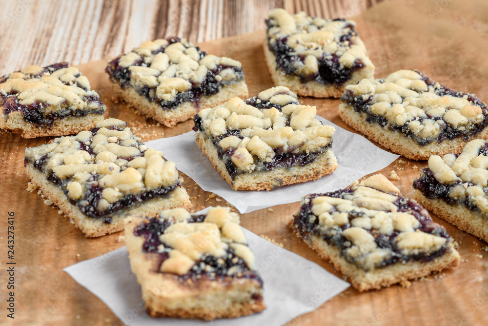 Shortbread cookies with blueberry jam on baking paper on wooden background. 
