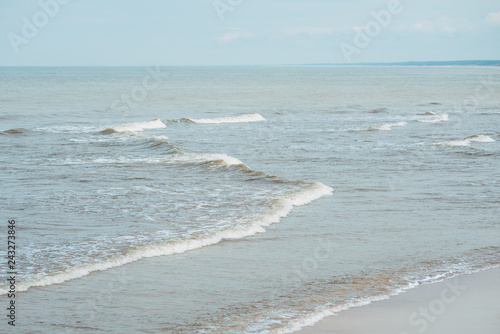 Sandy beach and blue sea with waves and seafoam. Background image for travel, summer vacation, and recreation. Vivid photo of tropical paradise.