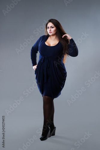Plus size fashion model in blue dress, fat woman on gray studio