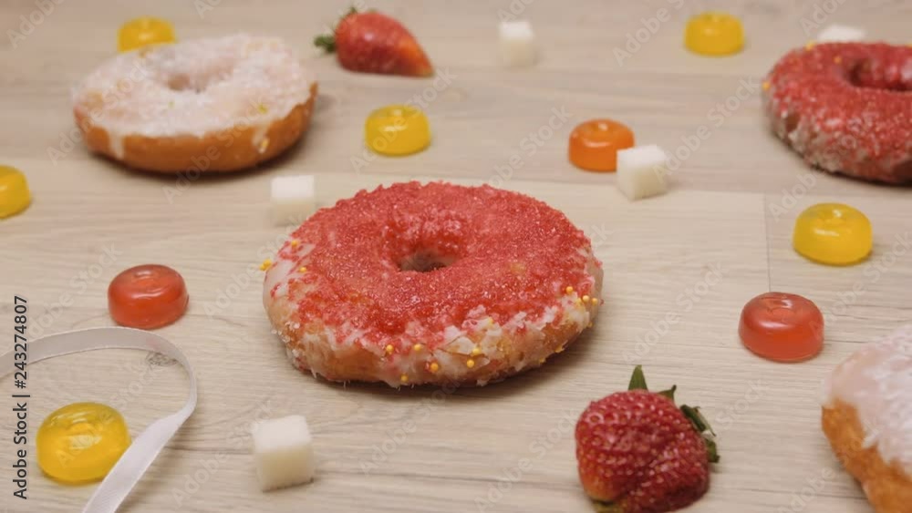 Donuts, sweetmeats candy and strawberry on wooden background. Background of coconut and berry homemade glazed and filled donuts. Assorted colorful red and white sweet sugar donuts and sweets. Donuts, sweetmeats candy and strawberry on wooden background. Background of coconut and berry homemade glazed and filled donuts. Assorted colorful red and white sweet sugar donuts and sweets.