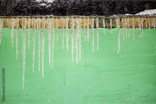 A lot of frozen icicles against the background of a green wall