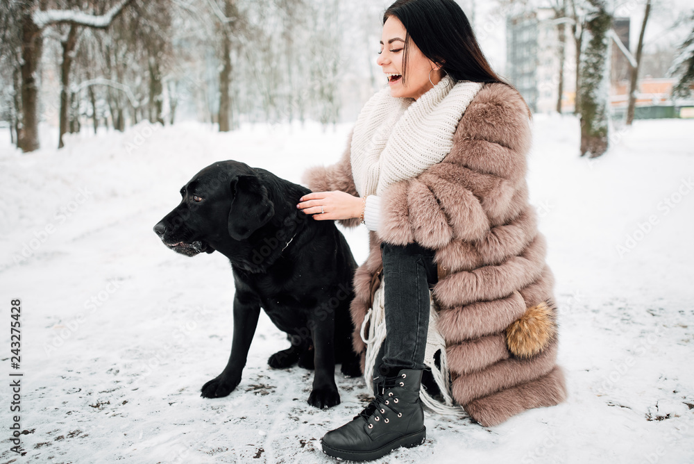 beautiful young girl with black hair in fur coat in winter outdoors, woman with big dog .snowy frosty day beautiful young girl with black hair in fur coat in winter outdoors, woman with big dog .snowy frosty day