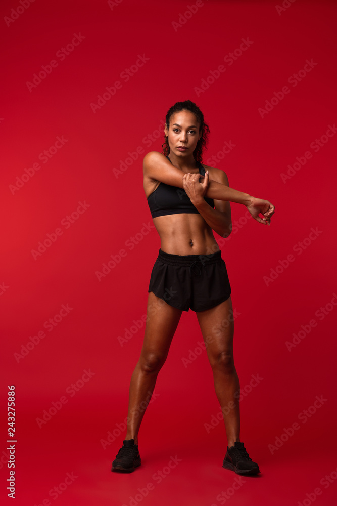 Strong young african sports fitness woman posing isolated over red wall background make exercises. Strong young african sports fitness woman posing isolated over red wall background make exercises.