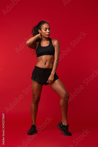 Beautiful young african sports fitness woman posing isolated over red wall background. © Drobot Dean