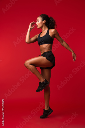 Strong young african sports fitness woman posing isolated over red wall background make exercises. © Drobot Dean