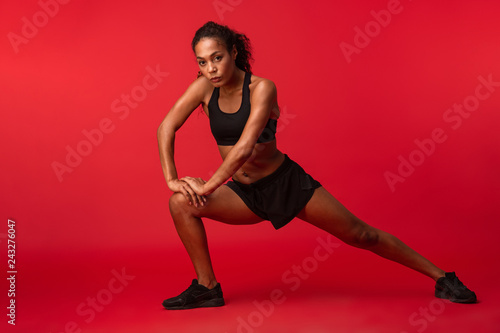Fototapeta Naklejka Na Ścianę i Meble -  Strong young african sports fitness woman posing isolated over red wall background make exercises.
