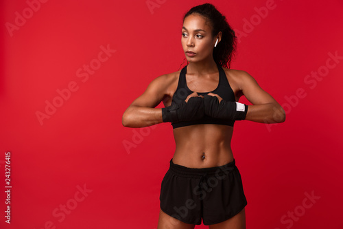Image of feminine african american woman in black sportswear wearing sports bandages on her hands, isolated over red background © Drobot Dean